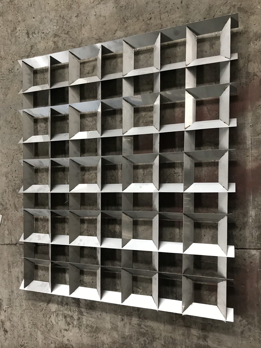 Stainless steel flocculation grid panel standing against a concrete wall